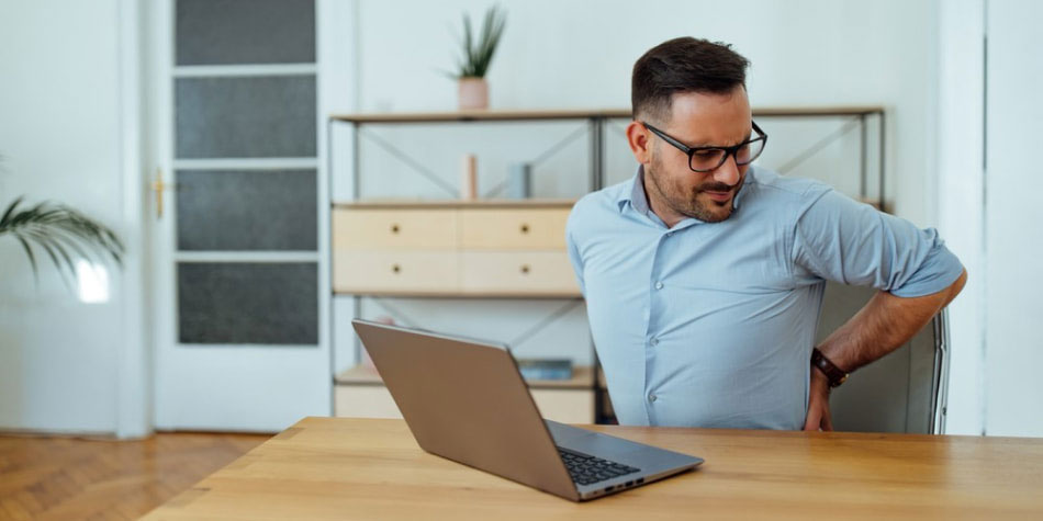 Man sitting at desk touching his back in pain